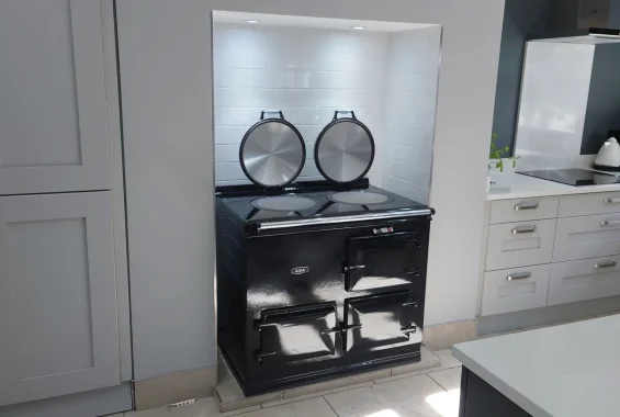 Sleek black aga cooker fitted in a modern white-tiled kitchen alcove with minimalist grey cabinetry and a clean countertop. A perfect combination of style and functionality at John Wray Range Cookers