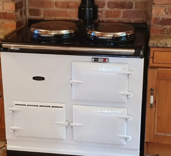 White 2-oven aga cooker installed in a rustic kitchen with exposed brick wall and wooden cabinetry, showcasing a classic and timeless aesthetic by John Wray Range Cookers.
